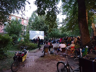 etwa 70 bis 80 Personen schauen in der Dämmerung einen Film
