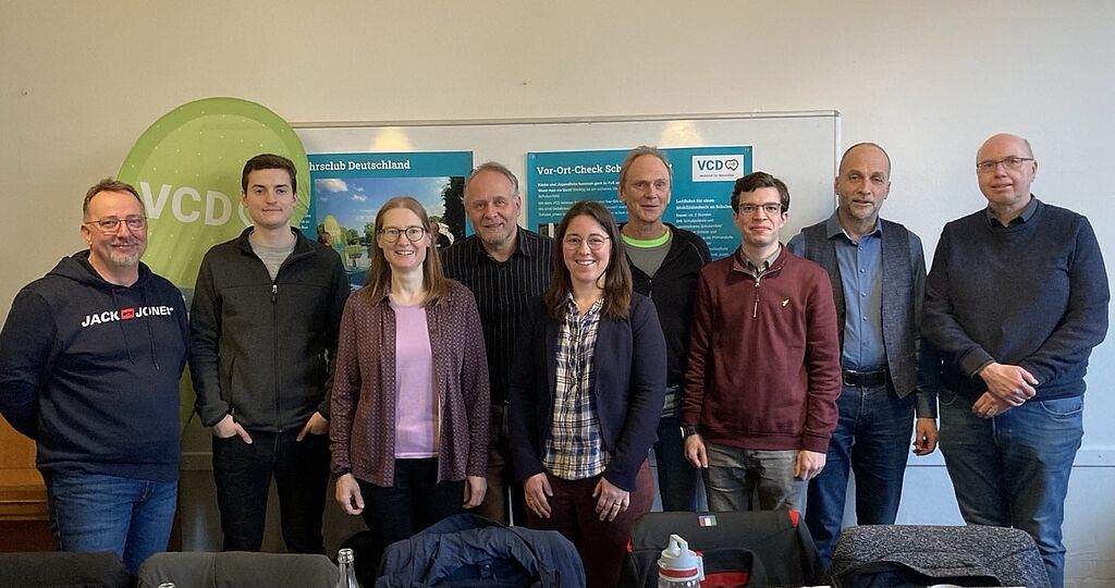 Neun Menschen stehen in einem Gruppenfoto. Im Hintergrund eine VCD-Flagge.