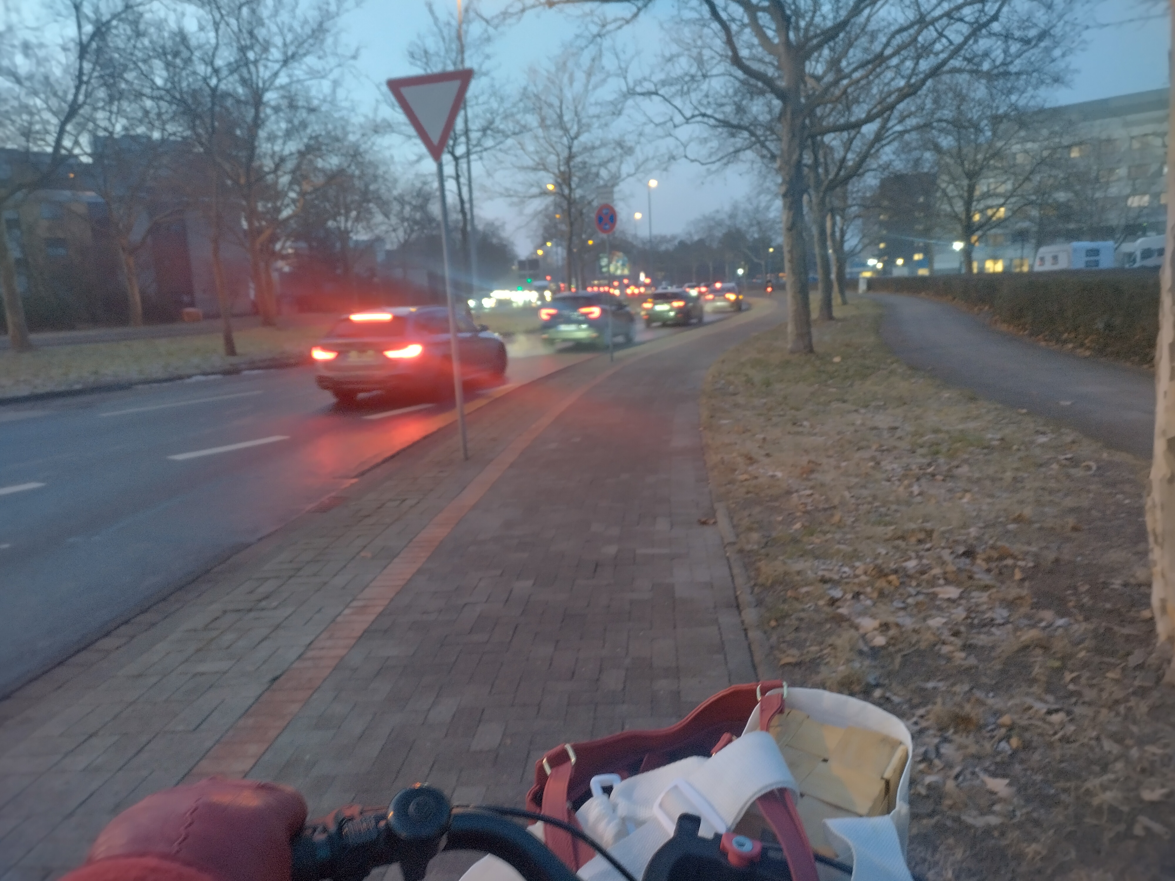 Blick vom abgetrennten Fahrradweg auf eine mehrspurige straße in der Dämmerung. Man sieht rote Rücklichter...